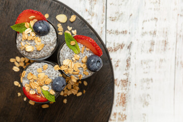 Chia seed pudding shots with fruit and granola on wooden board.