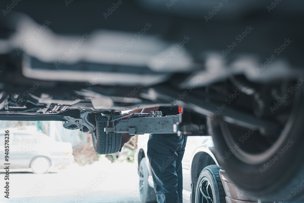 Poster close-up view of a mechanic examining a car's undercarriage while it is lifted for maintenance or re