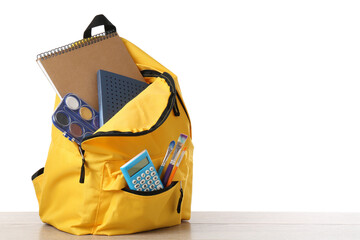 Backpack with different school stationery on wooden table against white background, space for text