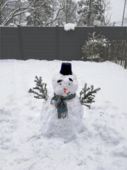 Funny snowman in black heat and blue scarf in the garden in winter. Ready for Christmas,...