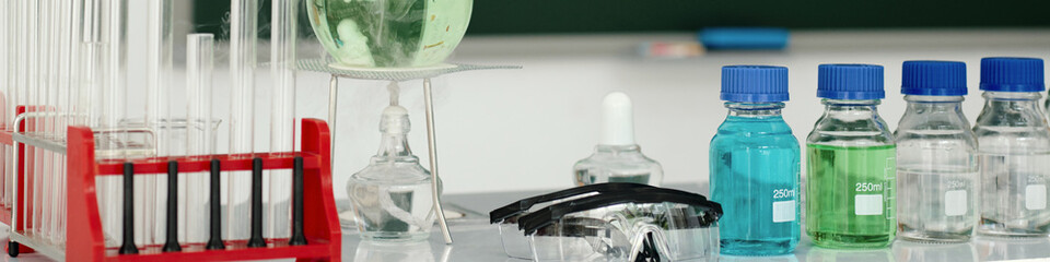 Collection of laboratory glassware including beakers and test tubes arranged on benchtop with various colored liquids inside glass containers creating a scientific environment