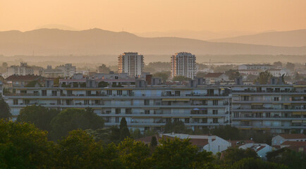 Obraz premium Evening view of the city of Perpignan, France, sunset, haze, red roofs, houses, trees, life, vacation, postcard, Europe, mountain silhouettes, calm, beauty, summer