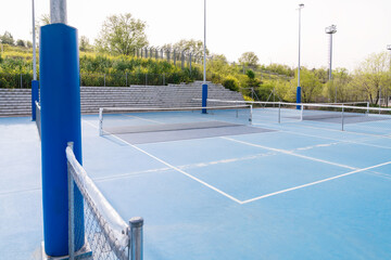 Outdoor pickleball court with blue flooring and surrounding greenery, empty and ready for play.