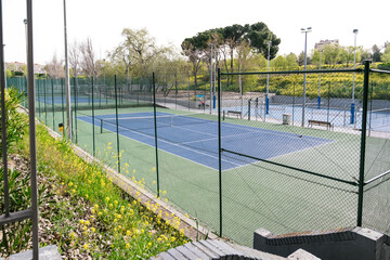 View of fenced tennis courts with surrounding greenery in a sports complex