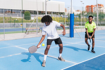 Two African teammates strategizing and enjoying a fun game of pickleball on a bright, sunny day.