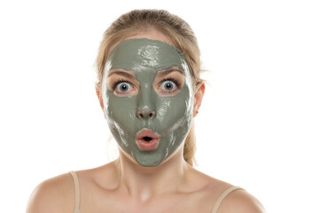 Beautiful funny young woman posing with a facial green mud mask on her face. Skin care and treatment, spa, natural beauty and cosmetology concept