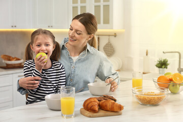 Mother and her cute little daughter having breakfast at table in kitchen on sunny morning