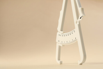 Plastic body fat caliper on beige background, closeup. Space for text