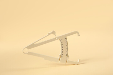 Plastic body fat caliper on beige background