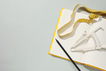 Body fat caliper, measuring tape and notebook on grey background, flat lay. Space for text
