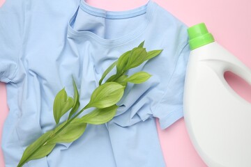 Bottle of laundry detergent, t-shirt and green branch on pink background, flat lay