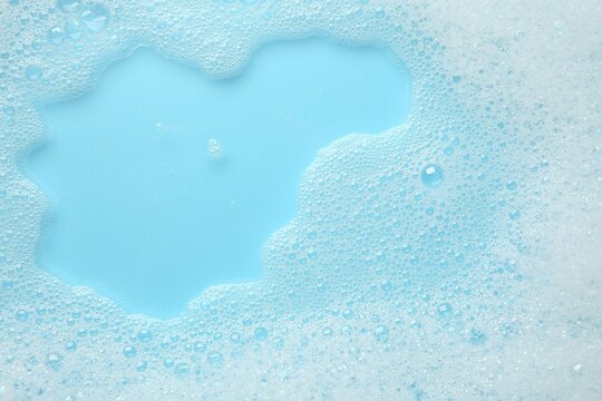 Washing laundry. White foam with bubbles on light blue background, top view