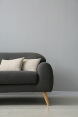 Comfortable sofa with cushions near grey wall in room, space for text