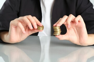 Financial inequality. Woman comparing two stacks of coins at table, closeup