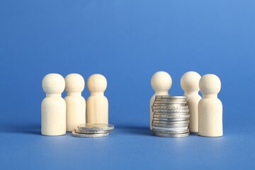 Financial inequality. Wooden figures and stacked coins of different height against blue background