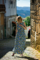 A woman in a summer dress stands on a narrow cobblestone street in an old town.
