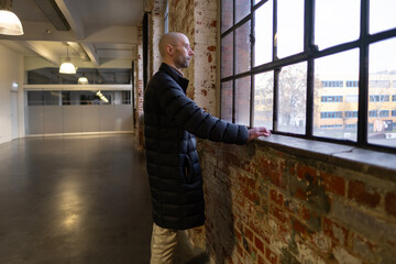 Fototapeta premium pensive romantic young man, in quilted jacket gazes thoughtfully out window, lost in deep thought about lifeeyes, reflecting on life’s moments