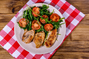 Roasted chicken breasts and salad with arugula and cherry tomatoes in a ceramic plate. Top view
