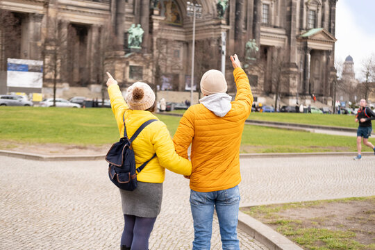 mature couple walking around berlin with phone, wearing vibrant yellow jacket and enjoying city's atmosphere, Traveler captures Berlin's essence, leisurely walk through