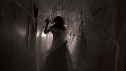 Woman in white dress looking like a ghost carelessly walking the hallway of a haunted house. Horror movie