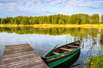 Obraz premium Wooden pier and fishing boat on shore of beautiful lake at sunrise, Suwalski Landscape Park, Podlasie, Poland