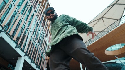 Low angle view of hipster pose in hip hop style surrounded by mall view. Portrait of sporty asian hip hop choreographer dancing break dance while looking at camera. Outdoor sport 2024. Hiphop.