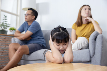 Scared little girl close her ears while her parent are having a fight in the livingroom