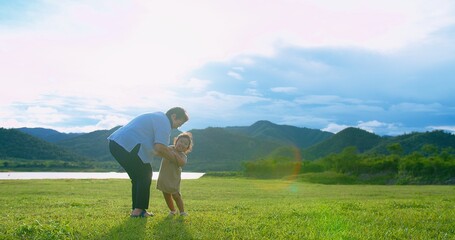 A joyful moment of a happy Asian grandmother lifting her grandchild in the air with smile against a beautiful Outdoors mountain and lake landscape under a bright sunny sky