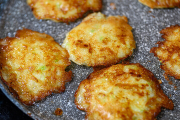 Making zucchini pancakes on a plate with oil squirting on a plate. Coocking at home concept.