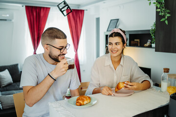 Two friends male and female are eating croissant for breakfast