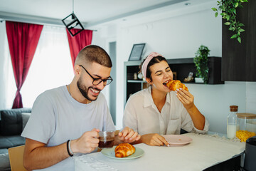 Two friends male and female are eating croissant for breakfast