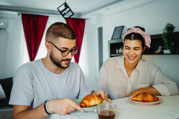 Two friends male and female are eating croissant for breakfast