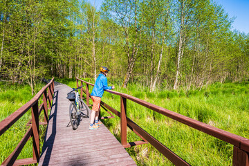 Fototapeta premium Woman cyclist standing on wooden bridge on shore of Wigry lake, Wigry National Park, Podlasie, Poland