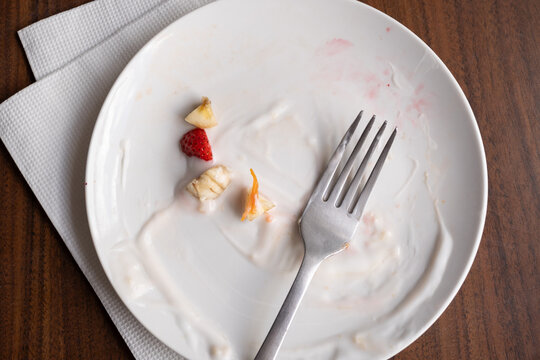 Plato vac&iacute;o terminando de desayunar con tenedor y restos de yogurt y fruta