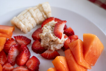 fruta picada en plato blanco para desayuno con avena, fresa, papaya  y plátano