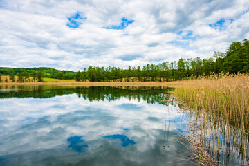 View of beautiful Kamedul lake and green hills in background and cloudy sky, Suwalski Landscape Park, Podlasie, Poland