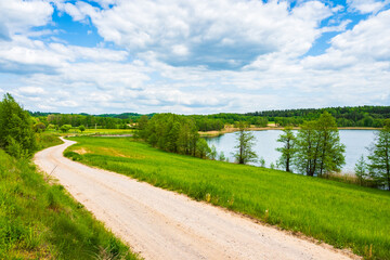 Countryside dirt road along green fields meadows and Kamedul lake, Suwalski Landscape Park, Podlasie, Poland