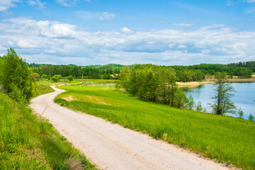 Countryside dirt road along green fields meadows and Kamedul lake, Suwalski Landscape Park, Podlasie, Poland