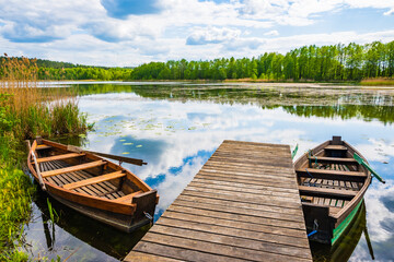 Obraz premium Fishing boats anchoring by wooden pier at beautiful lake, Suwalski Landscape Park, Podlasie, Poland
