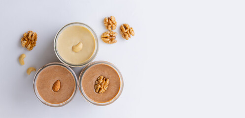 Three Urbech paste of almond, cashew, walnut nuts in glass jar on white background banner, top view