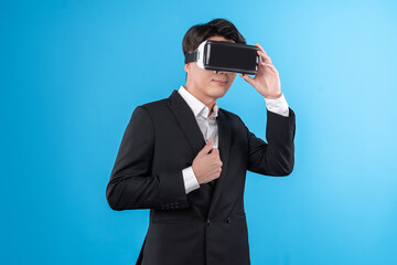 Smiling Asian businessman looking thorough VR connecting to business world report in futuristic metaverse, analyzing innovation technology ads in virtual reality isolated blue copyspace. Contrivance.