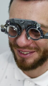 Handsome man at ophthalmology clinic. Special testing glasses with replacable lenses for vision correction on a male patient. Vertical video