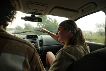 Young woman in casualwear pointing forwards and looking at male driver of pickup truck while sitting next to him during talk