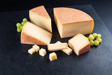 Traditional aged mountain cheese of the Alps offered as close-up with grapes on a design board