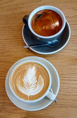 two cups with cappucino, latte art and black coffee on a wooden table