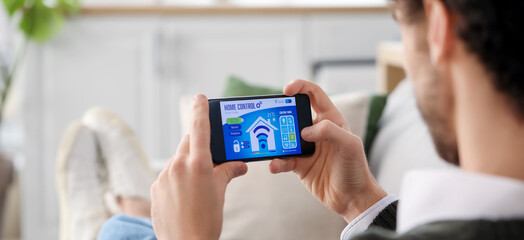 Young man using mobile phone with smart home security system control panel, closeup