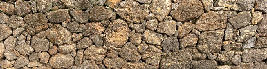 Wall texture with rough and natural old stones in various shades of brown, gray, and yellowish