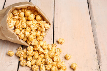 Paper bag with crispy popcorn on white wooden background
