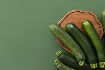 Wooden board with many fresh zucchini on green background