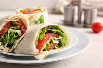 Plates of tasty lavash rolls with tomatoes and greens on light background
